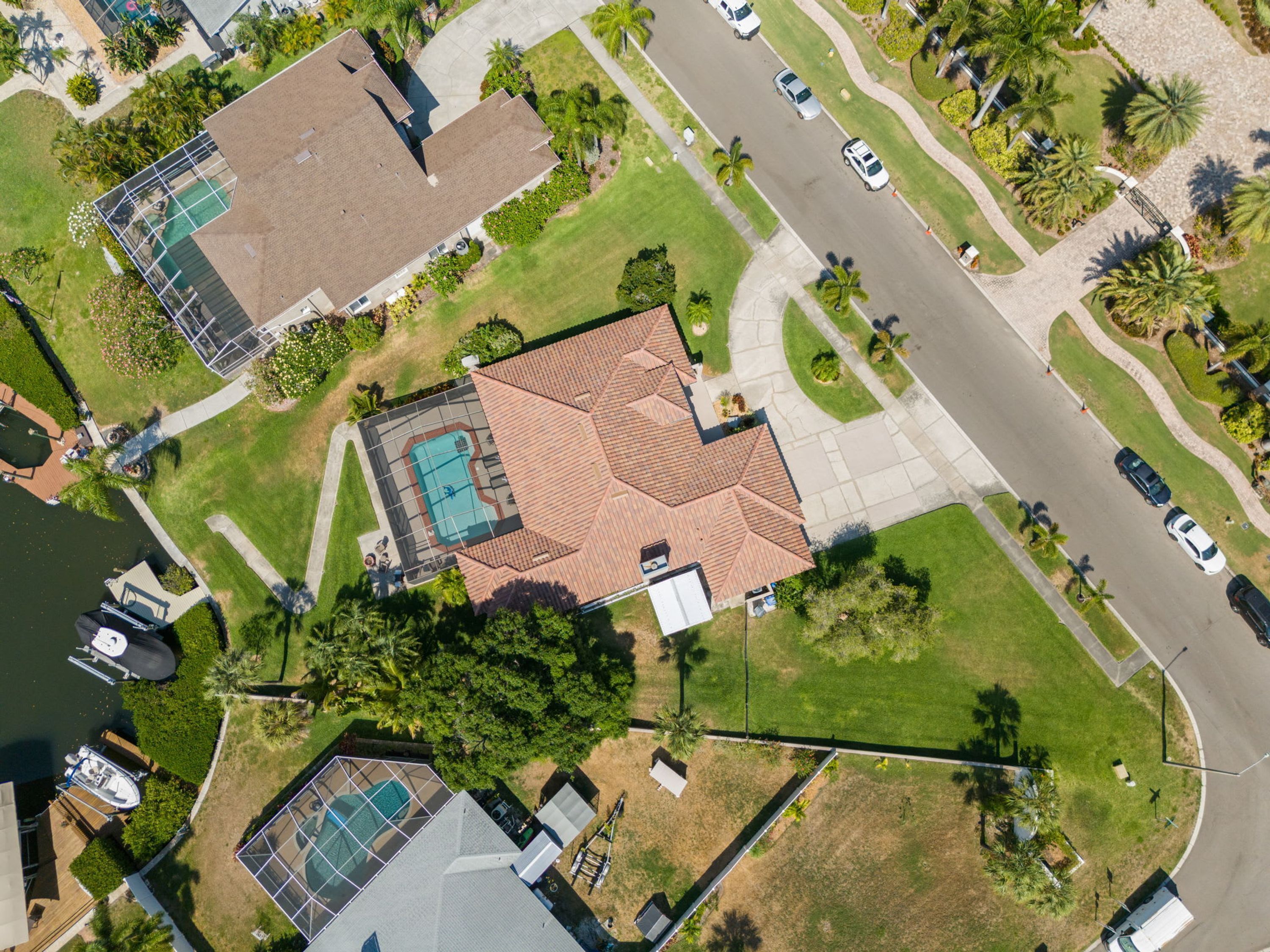 An aerial view of a residential area with a house featuring a swimming pool, a tennis court, and a well-maintained lawn.