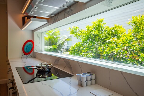 A kitchen with a modern stove, a window with a view of greenery, and a red and blue decorative plate on the wall. - NEW The Rigby House - Pvt Pool Amazing Location (Key West)