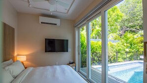 A bedroom with a large bed, a flat-screen TV mounted on the wall, and a window overlooking a swimming pool. - NEW The Rigby House - Pvt Pool Amazing Location (Key West)