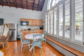 A kitchen with wooden cabinets, a stainless steel refrigerator, a microwave, and a dining area with a round table and chairs. - New Rose Retreat - Pool Parking (Key West)
