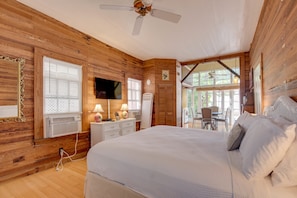 A wooden-paneled bedroom with a large bed, a ceiling fan, a TV, and a view of the outdoors. - New Rose Retreat - Pool Parking (Key West)