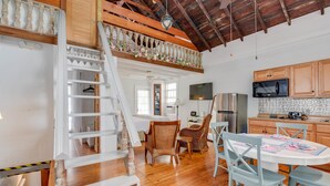 A spacious kitchen with wooden cabinets, a dining area with wicker chairs, a staircase with a railing, and a TV mounted on the wall. - New Rose Retreat - Pool Parking (Key West)