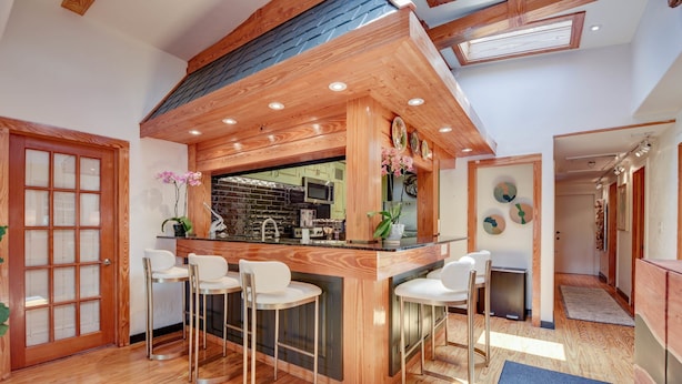 Une cuisine moderne agrémentée d’éléments en bois, un coin bar avec des tabourets et une vue sur la salle à manger adjacente.