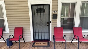 A front porch with a black metal door, a welcome mat, and two red chairs. - Charming 3-bedroom house with AC and WiFi in welcoming Mobile (Mobile)