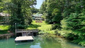 A house surrounded by lush greenery and a calm body of water with a dock. - Living the Dream- Lakefront-Dock (Hiawassee)