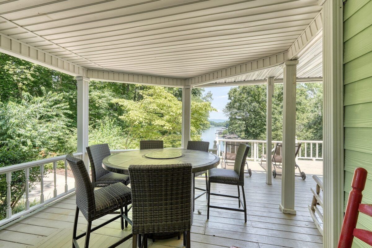 A covered outdoor area with a round table and wicker chairs, surrounded by a white railing.