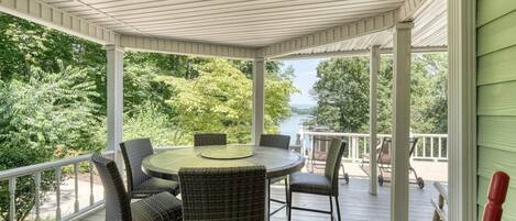 A covered outdoor area with a round table and wicker chairs, surrounded by a white railing.