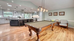 A spacious living area with a pool table, wooden flooring, and a kitchen in the background. - Living the Dream- Lakefront-Dock (Hiawassee)