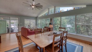 A spacious dining area with a wooden table and chairs, large windows offering a view of trees, and a ceiling fan. - Living the Dream- Lakefront-Dock (Hiawassee)