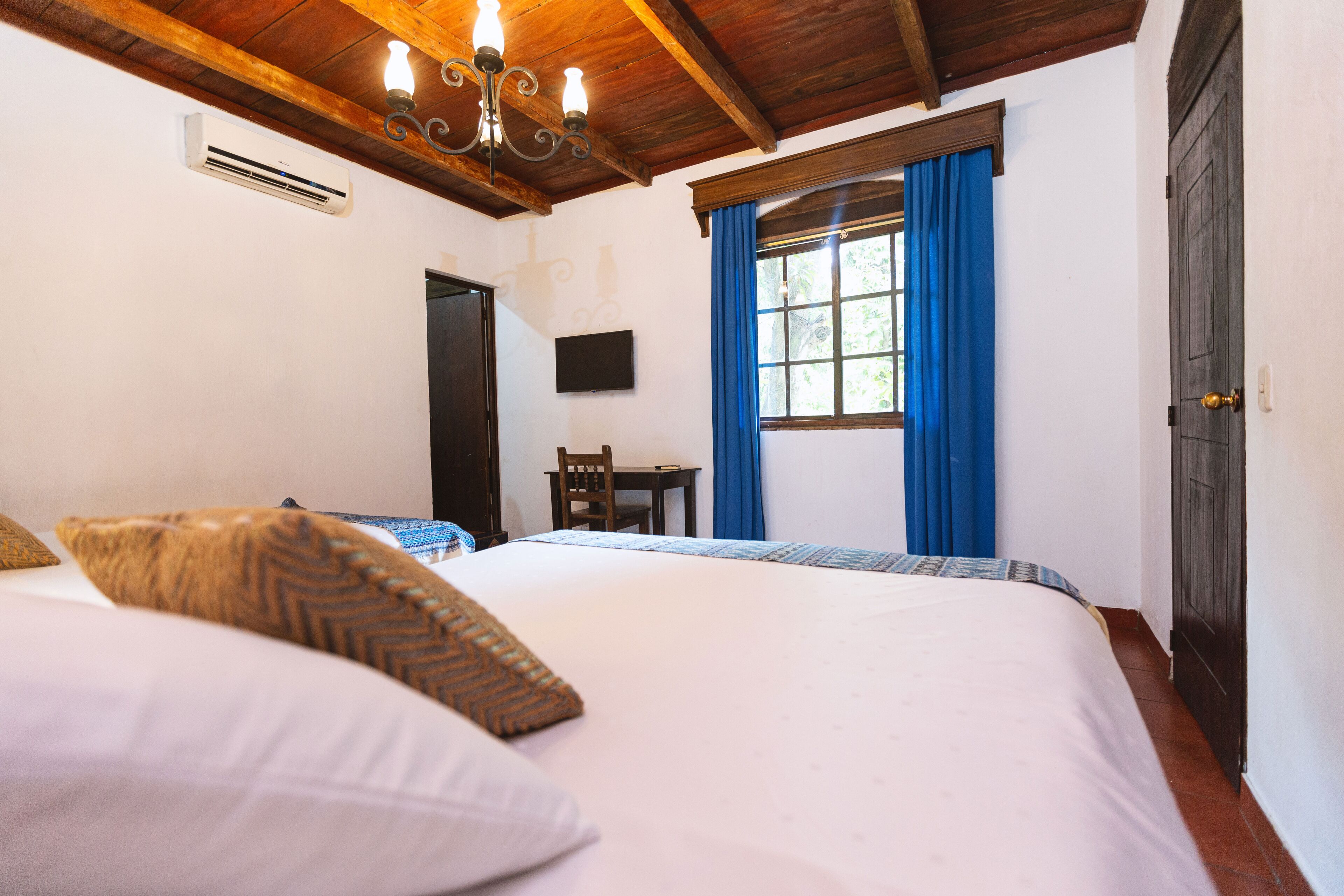 Een slaapkamer met een groot bed, een stoel, een televisie en een raam met gordijnen.