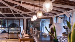 A modern bar area with wooden chairs, a counter, hanging pendant lights, and a potted plant. - Hotel Las Marias (Taxisco)