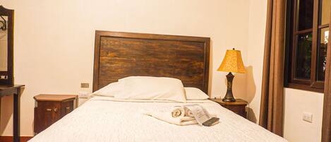 Una cama bien tendida con cabecera de madera, una lámpara de noche y una toalla doblada sobre la cama.