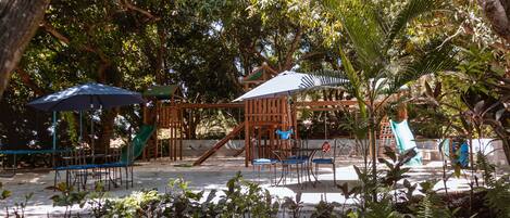 Un parque infantil con toboganes y estructuras para escalar, rodeado de árboles.