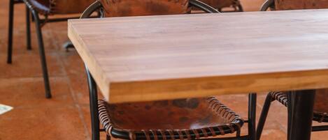 A series of wooden tables and wicker chairs arranged outdoors, likely in a patio or garden area.