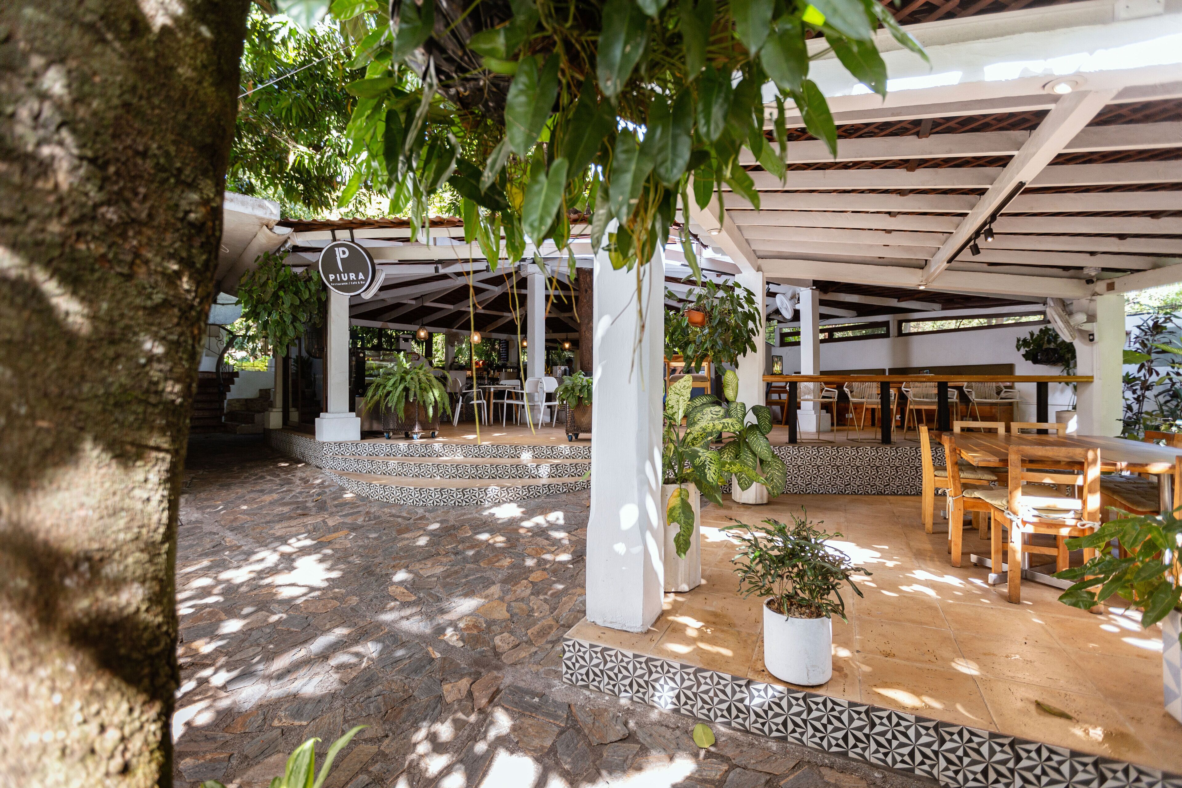 An outdoor patio area with stone flooring, wooden tables and chairs, and potted plants.