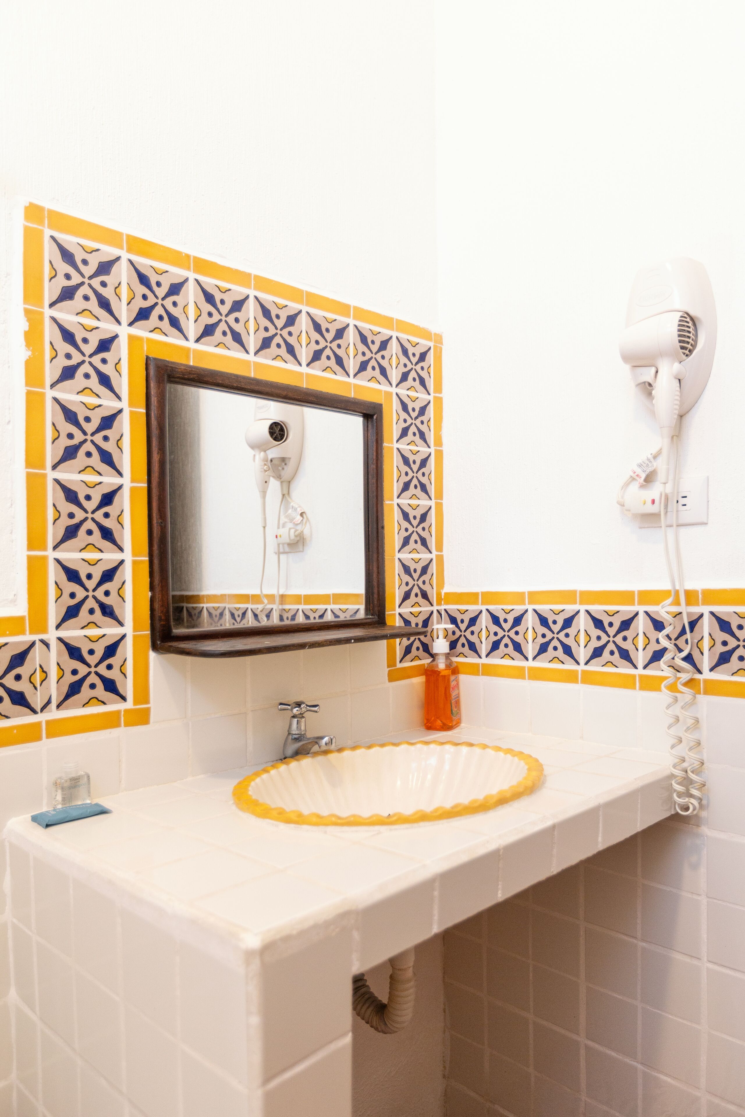 A bathroom with a sink, mirror, and a hairdryer mounted on the wall.