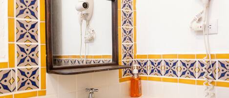 A bathroom with a sink, mirror, and a hairdryer mounted on the wall.