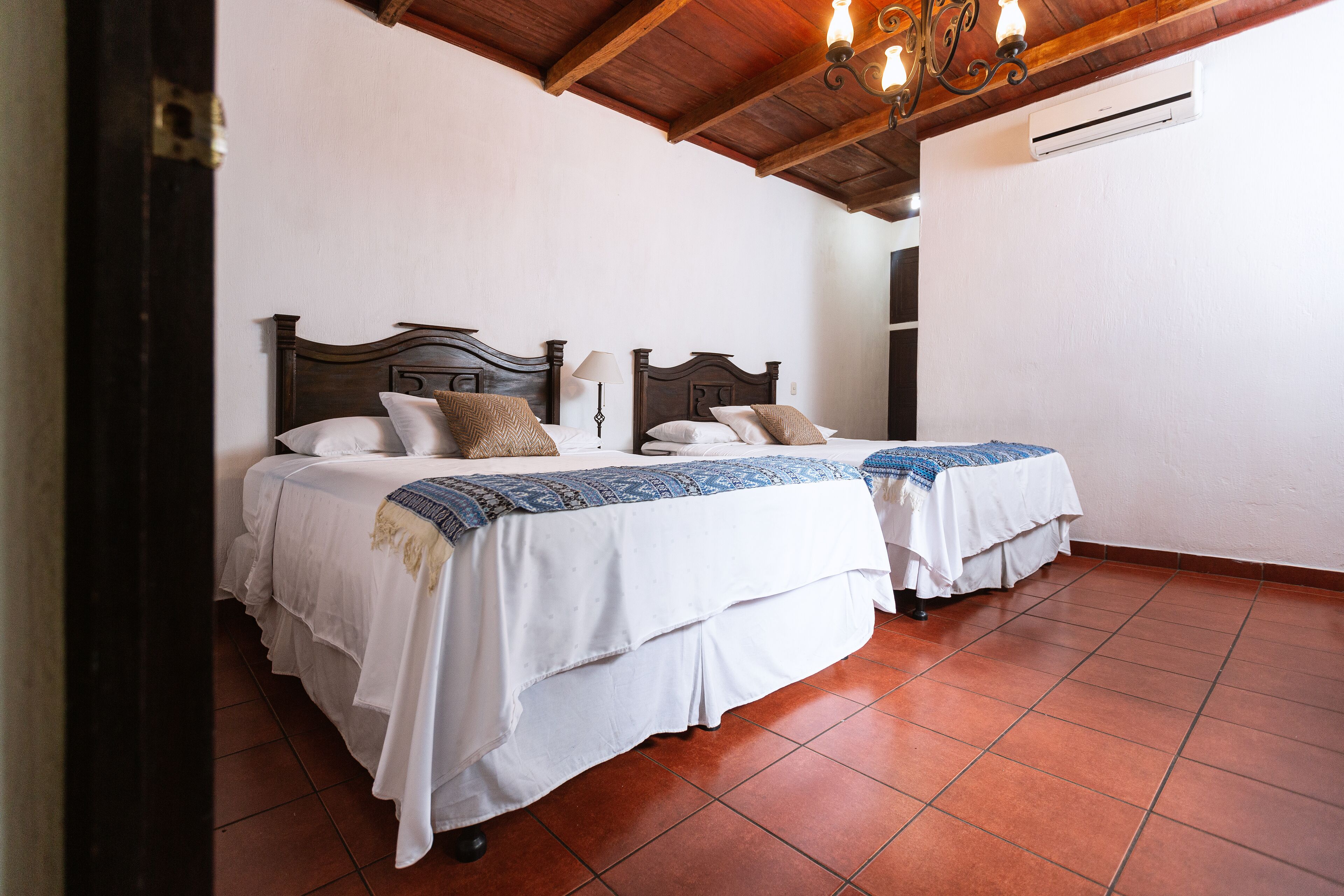 A room with two beds, white bedding, and a wooden ceiling.
