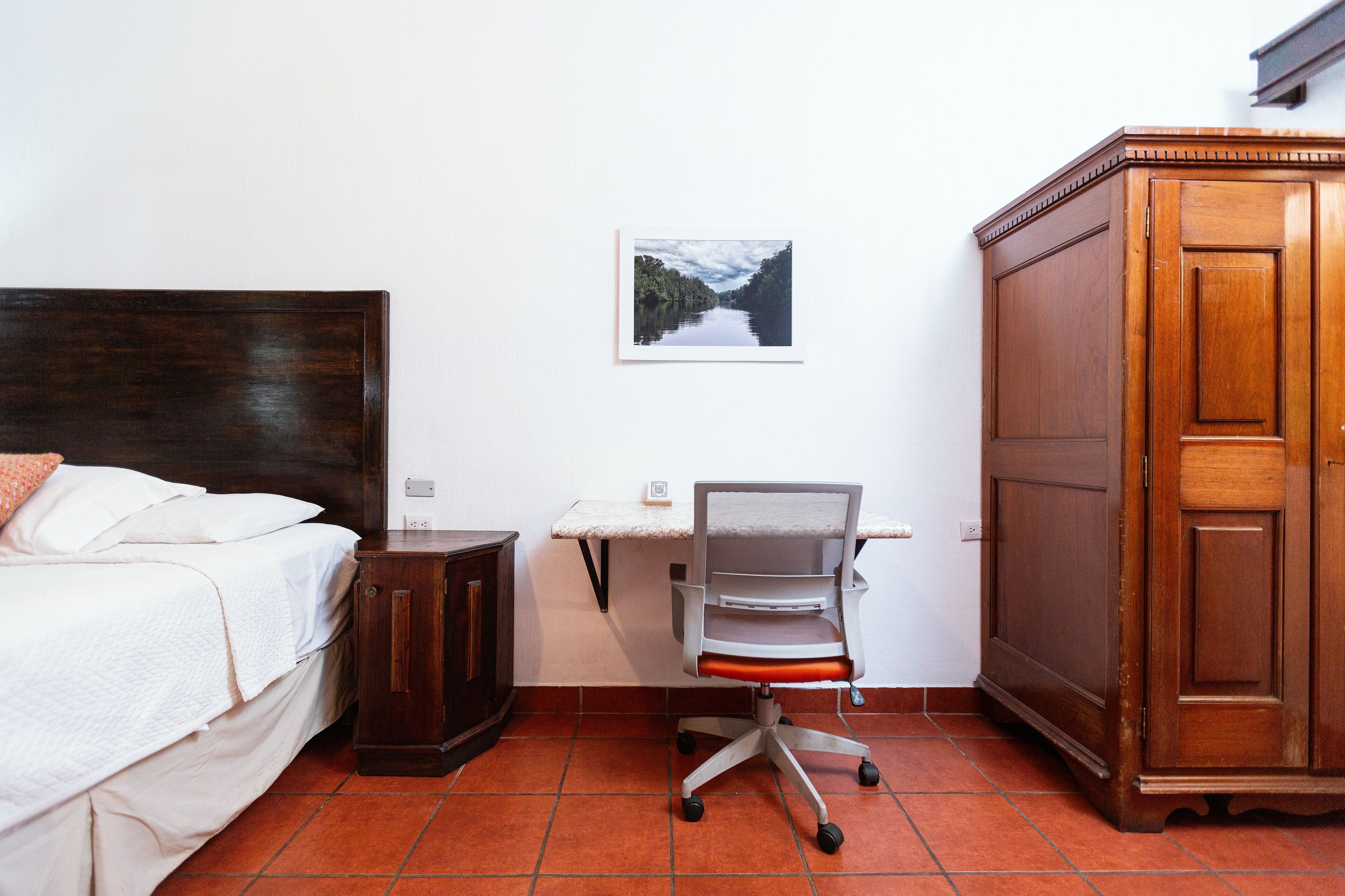 Un dormitorio con cama, escritorio con silla, armario y un cuadro en la pared.
