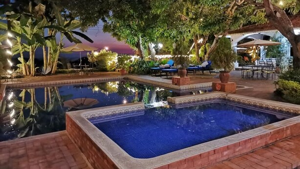 A nighttime pool area with a clear pool, surrounding plants, and lounge chairs. - Hotel Las Marias (Taxisco)