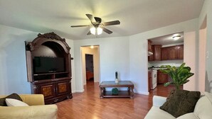 Ein Wohnzimmer mit Fernseher, Sofa, Couchtisch und Deckenventilator.
