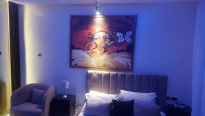 A modern bedroom with a large bed, a headboard, a chair, bedside tables, and a wall-mounted artwork. - Beautiful 2-bed Apartment in Lekki (Lekki)