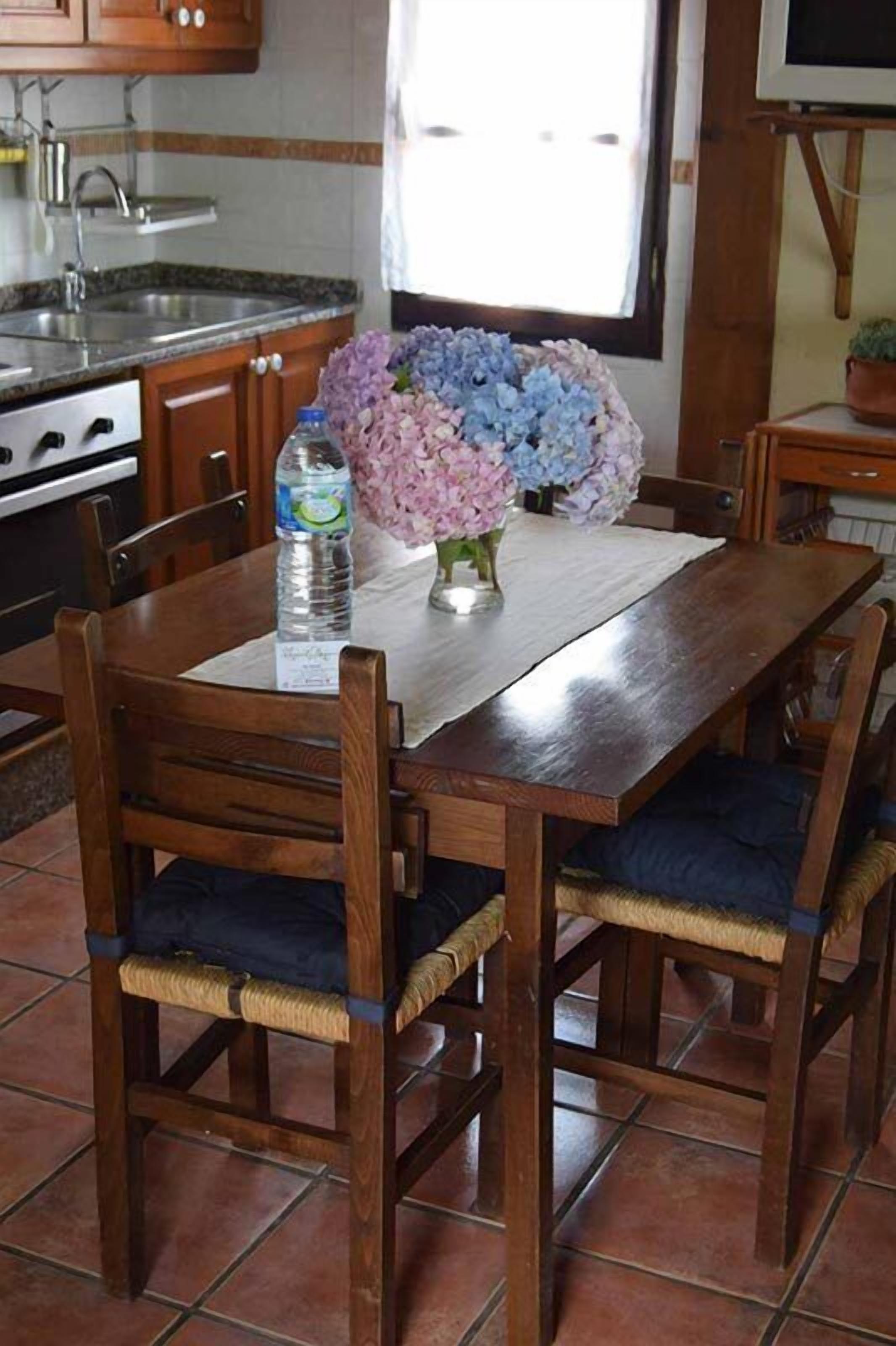 A dining table with chairs, a vase of flowers, and a water bottle.