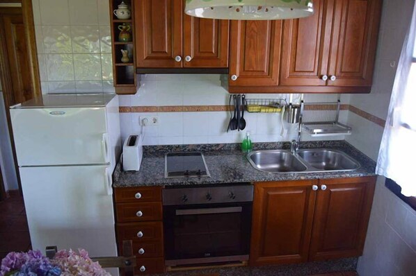Una cocina compacta con armarios de madera, horno empotrado, lavamanos y refrigerador.