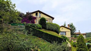 Una casa en la ladera con fachada de piedra, escalera de madera y un jardín con bancos.