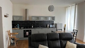 Una cocina moderna con gabinetes grises, una campana extractora de acero inoxidable y una zona de comedor con un sofá de cuero negro y dos sillas.