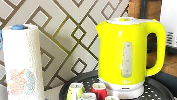 A kitchen area with a yellow kettle, a roll of paper towels, and colorful mugs on a tray.
