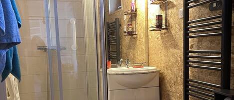 Un baño con cabina de ducha de vidrio, un lavabo blanco y un perchero para toallas.