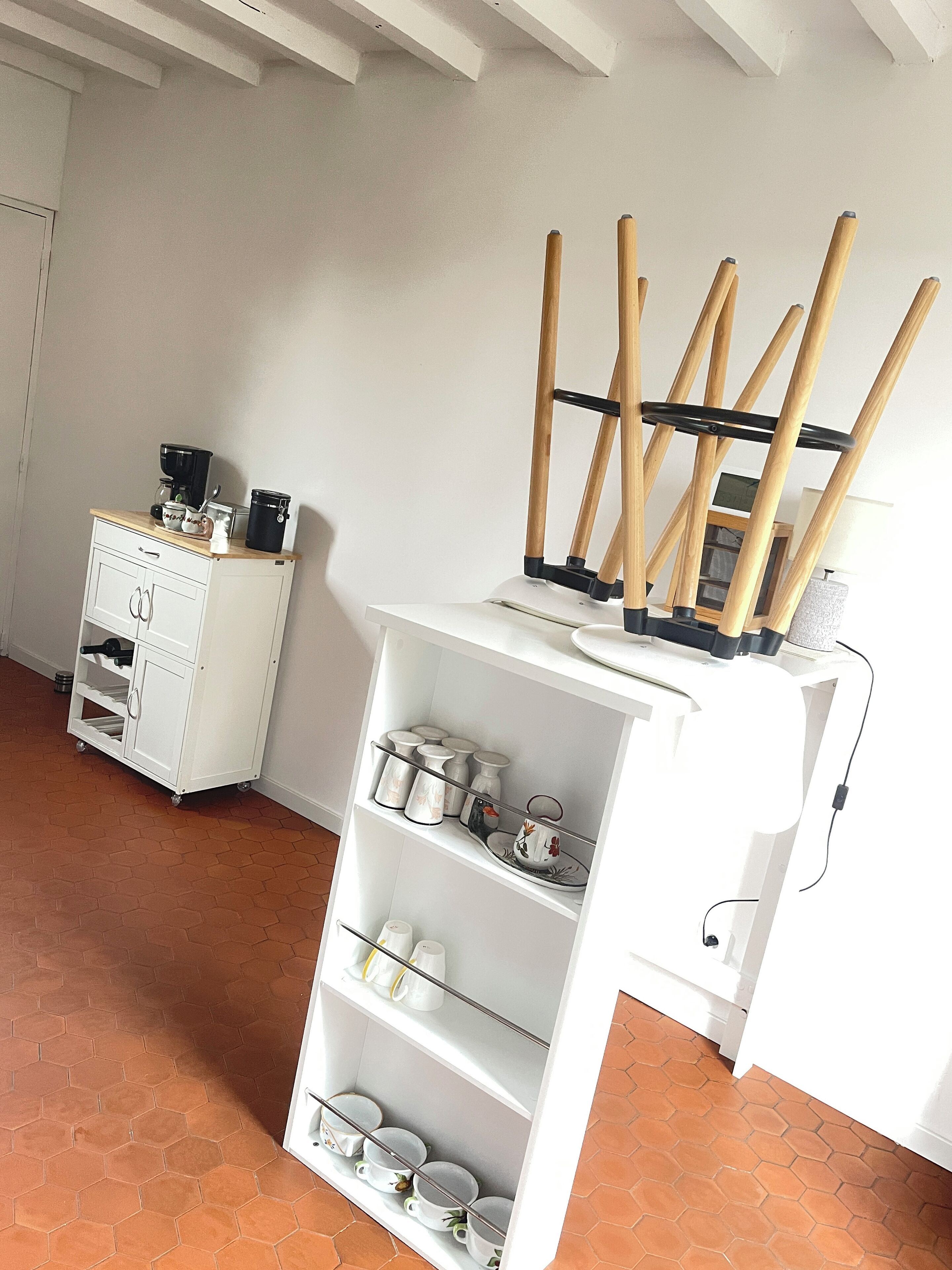 Una cocina con un armario blanco, una cafetera y una estantería con utensilios de cocina.