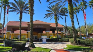 Un hotel con techo de tejas rojas, palmeras y un jardín bien cuidado.