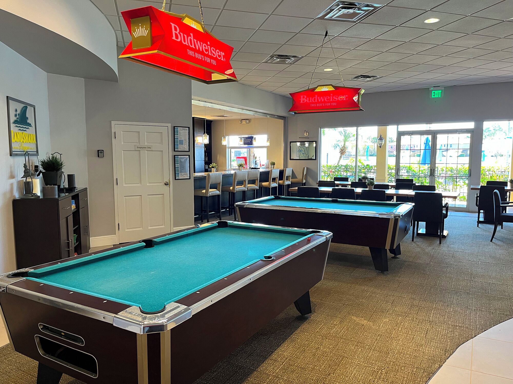 A pool hall with multiple pool tables, a bar area, and a view of the outdoors through large windows.