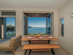 A dining area with a table set for two, a bench, and a view of the sea. - Hahei Oceanfront - Hahei Holiday Home (Hahei)