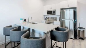 A modern kitchen with a central island, stainless steel appliances, and grey bar stools. - Spacious 3BR+Den with Hot Tub,  Near Disney! (Davenport)
