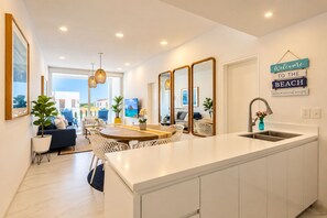 Et moderne køkken med en central ø, et spiseområde med et rundt bord, og en opholdsstue med sofa og stole.