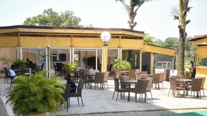 An outdoor cafe area with tables and chairs, a large potted plant, and a pool. - WestPoint Hotels Limited (Abuja)