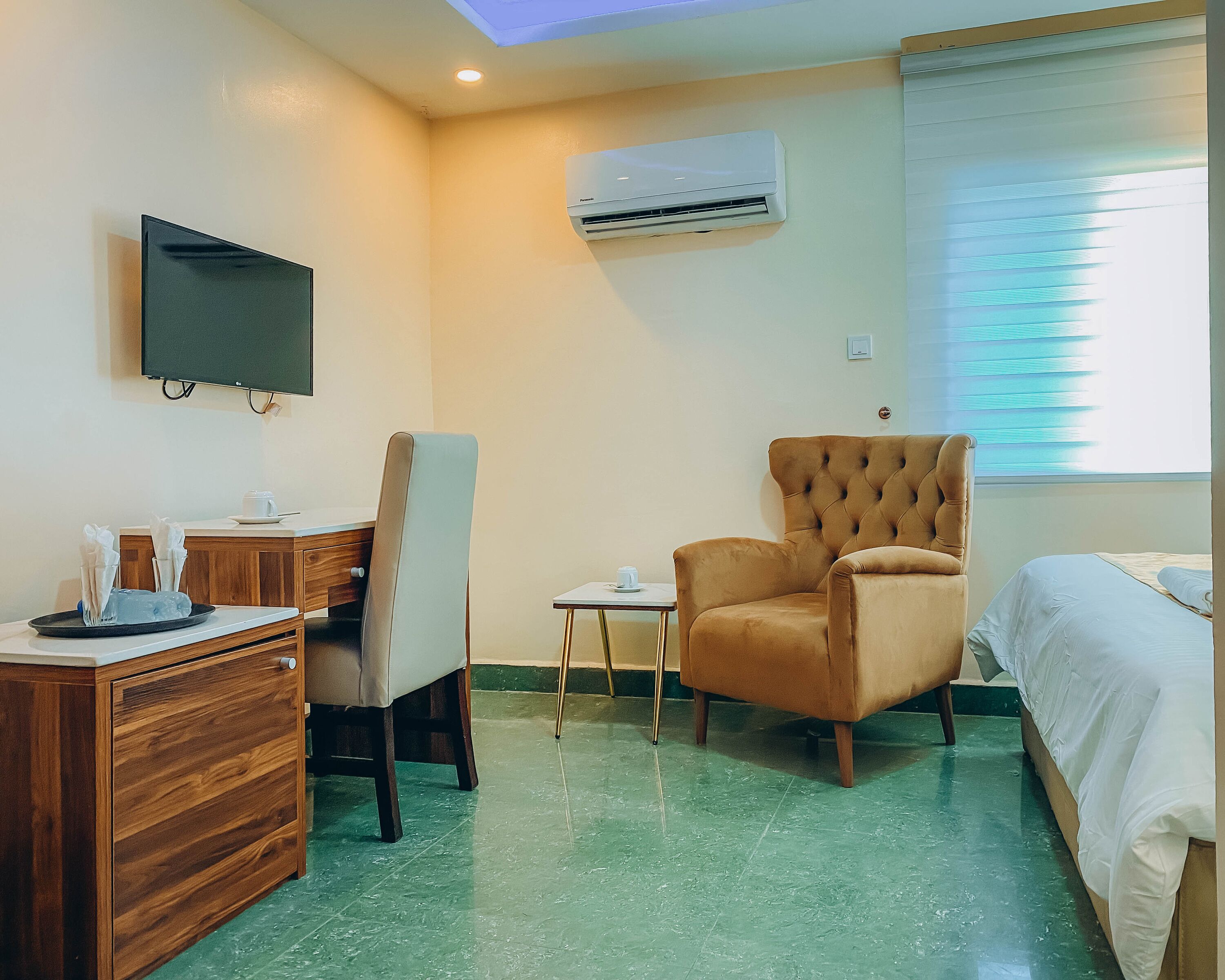 Ein Hotelzimmer mit einem Bett, einem großen Sessel, einem Schreibtisch mit Computer, einem Fernseher und einer Klimaanlage.