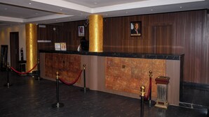 A reception area with a wooden panel wall, a gold-colored column, and a red velvet rope barrier. - WestPoint Hotels Limited (Abuja)