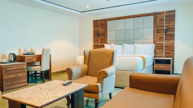 A modern hotel room with a bed, a desk, a chair, a sofa, and a small table. - WestPoint Hotels Limited (Abuja)