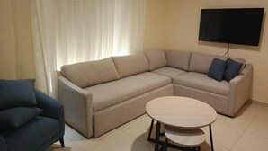 Un saló amb un sofà seccional beix, una taula de centre rodona i un televisor de pantalla plana fixat a la paret.