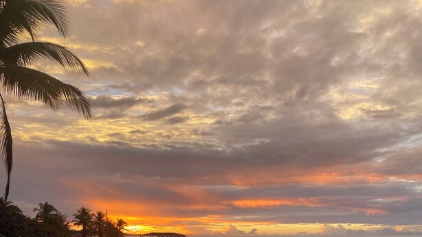 Una piscina con vistas a la puesta de sol sobre el océano, palmeras y una pequeña estructura sobre pilotes.