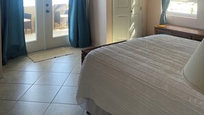 Un dormitorio con cama, ventilador de techo, puerta corrediza de vidrio que da a un balcón y ventana con cortinas.