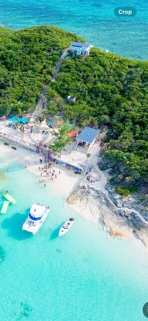 An aerial view of a coastal area with a beach, boats, and a small building surrounded by greenery.