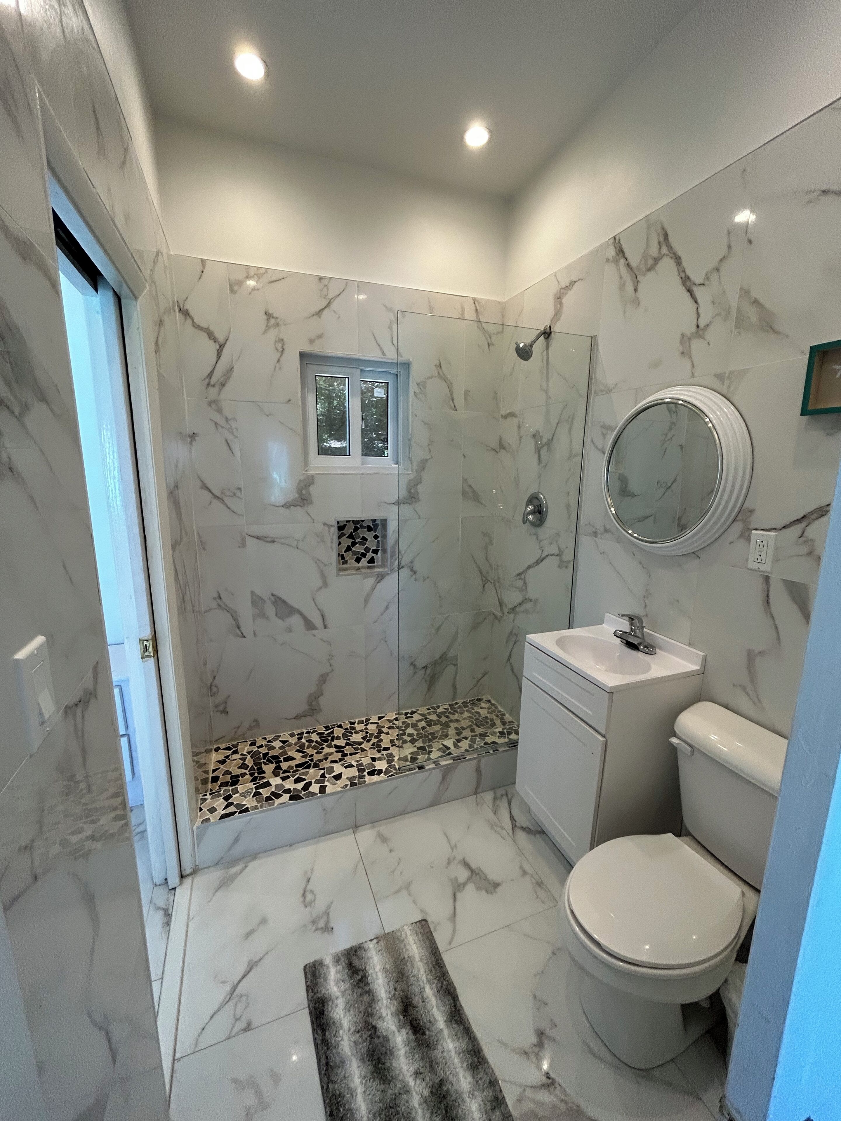 Une salle de bain avec une douche, des toilettes, un lavabo et une petite fenêtre.