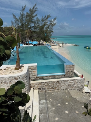 Ein Pool mit Steinrand, ein Strand und ein freier Blick auf den Ozean.
