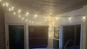 A room with a hot tub, string lights, and a window with blinds. - Green Acres (Minford)