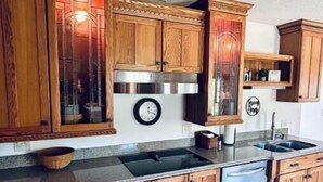 A kitchen with wooden cabinets, a stainless steel range hood, a clock, and a dishwasher. - Green Acres (Minford)